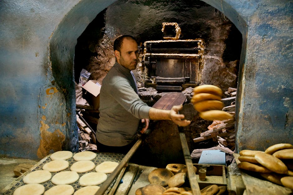 A baker uses a wooden paddle to remove freshly baked bread from a traditional oven.